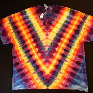 May include: A tie-dye t-shirt with a vibrant color scheme, featuring shades of red, orange, yellow, blue, and purple. The shirt has a V-shaped design with a symmetrical pattern.