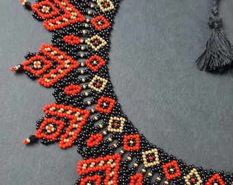 May include: A black, red, and gold beaded necklace with a geometric pattern. The necklace has a tassel at the end.
