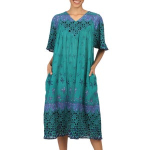 Puede incluir: Un vestido de estampado floral azul verdoso y morado con cuello de encaje y mangas cortas. El vestido tiene bolsillos a los lados y una silueta fluida.