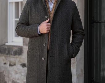 Puede incluir: Un abrigo gris oscuro con patrón de espiga, cuello alto, mangas largas y tres botones frontales. Debajo, un suéter color canela con cremallera sobre una camisa de botones a cuadros azules y blancos, junto con pantalones de cuadros marrones.