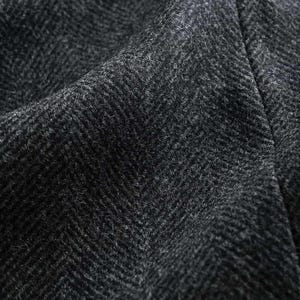 May include: Close-up of a dark gray herringbone fabric. The material has a textured surface with a diagonal weave pattern. The fabric is likely wool or a wool blend, suitable for jackets or coats. The words "Scottish Kilts & Jackets" are visible.