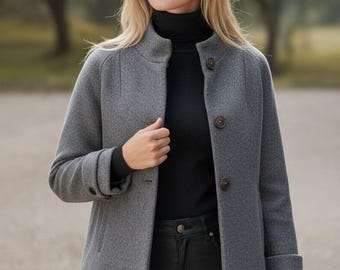 May include: A gray wool jacket with a mandarin collar and three brown buttons. The jacket is worn over a black turtleneck and paired with black pants. A logo is visible in the upper left corner.