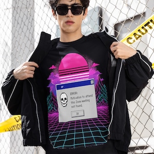 May include: Black graphic t-shirt featuring a retro sunset design and a computer error message: "ERROR: Motivation to attend this Zoom meeting not found." The shirt is worn with a black jacket.
