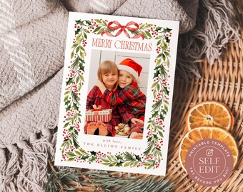 May include: A rectangular Christmas greeting card template featuring a watercolor holly and berry border with a red ribbon at the top. The card displays the text MERRY CHRISTMAS and with love, THE ELLIOT FAMILY, surrounding a central photo placeholder.