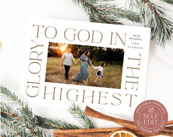 May include: A rectangular Christmas greeting card featuring a central photograph of a family walking in a field. The card displays the text TO GOD IN THE HIGHEST in large brown letters framing the photo, with MERRY CHRISTMAS, THE AITKENS printed.
