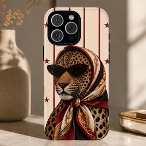 May include: A smartphone case featuring a leopard wearing dark sunglasses and a patterned headscarf in shades of red, gold, and white. The background of the case is cream-colored with vertical maroon stripes and small red stars scattered throughout.