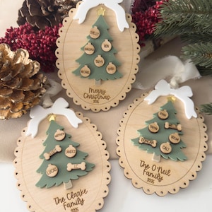 May include: Three wooden Christmas tree ornaments with scalloped edges and white bows. Each features a green tree with family names and the year 2025. One ornament has the text "Merry Christmas".