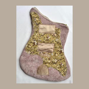 K&ouml;nnte beinhalten: Ein gitarrenf&ouml;rmiger Weihnachtsstrumpf. Der Strumpf hat ein Blumenmuster in der Mitte, mit einem hellbraunen Stoff an den R&auml;ndern. Er hat drei rechteckige Patches und einen kleinen bogenf&ouml;rmigen Patch.