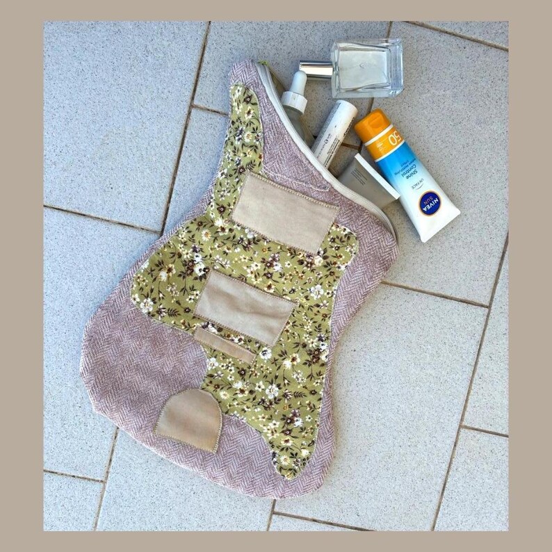 K&ouml;nnte beinhalten: Eine handgefertigte Kosmetiktasche in Form eines Gitarrenpicks. Die Tasche hat ein Blumenmuster, beige Patches und einen Fischgr&auml;tenstoff. Sie enth&auml;lt eine Parf&uuml;mflasche, Sonnencreme und andere Toilettenartikel.