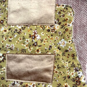 K&ouml;nnte beinhalten: Nahaufnahme eines Stoffst&uuml;cks mit einem Blumenmuster in Gr&uuml;n, Wei&szlig; und Braun. Es hat zwei rechteckige Patches aus beigem Samt. Der Rand eines rosa, strukturierten Stoffes ist sichtbar.