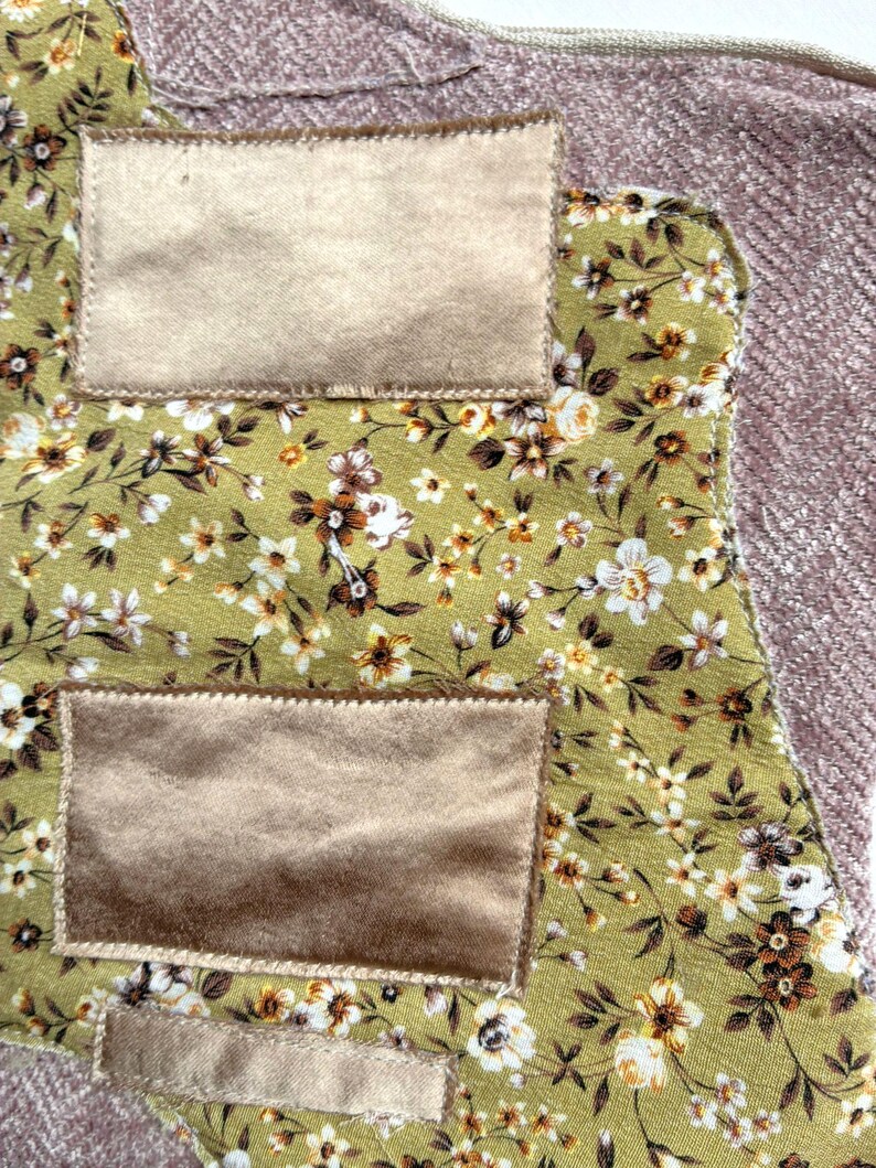 K&ouml;nnte beinhalten: Nahaufnahme eines Stoffst&uuml;cks mit einem Blumenmuster in Gr&uuml;n, Wei&szlig; und Braun. Es hat zwei rechteckige Patches aus beigem Samt. Der Rand eines rosa, strukturierten Stoffes ist sichtbar.