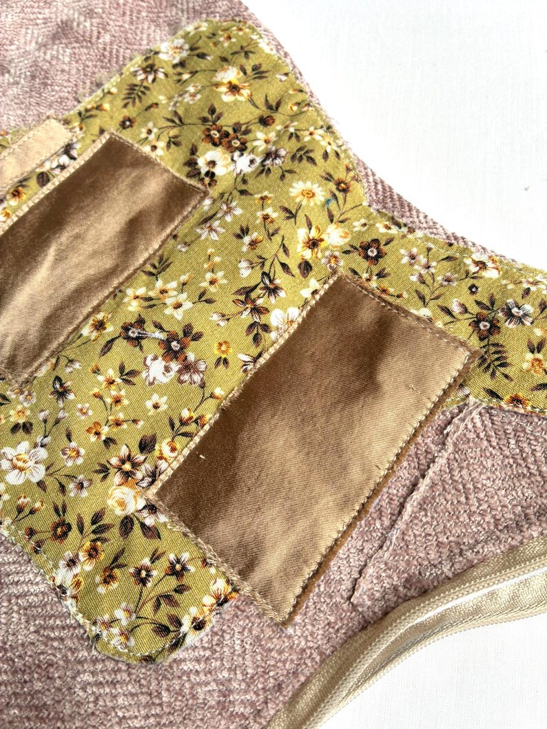 K&ouml;nnte beinhalten: Nahaufnahme eines handgefertigten Textilartikels mit einem floralen Muster in Gr&uuml;n, Braun und Wei&szlig;. Es hat rechteckige Patches in Beige und einen strukturierten rosa Hintergrund. Ein goldener Rei&szlig;verschluss ist sichtbar.