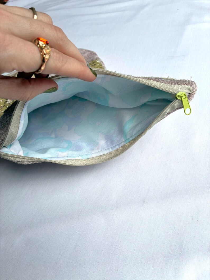 K&ouml;nnte beinhalten: Ge&ouml;ffnete, gezippte Tasche mit einem hellgr&uuml;nen Rei&szlig;verschluss. Die Au&szlig;enseite ist strukturiert und neutralfarben, w&auml;hrend die Innenseite ein hellblaues Blumenmuster aufweist. Die Tasche wird offen gehalten und zeigt das Innere.