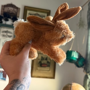 May include: A plush brown bunny toy with long ears and a fluffy white tail. The stuffed animal is made of soft, textured material and has a classic design, perfect for children or collectors.