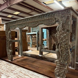 May include: A large, rectangular wooden console table featuring intricate hand-carved patterns across its front apron and sturdy legs. The wood has a weathered, distressed finish with muted grey and brown tones, showcasing detailed relief carvings.