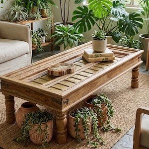 May include: A white ceramic mug with a black handle and the text "But First, Coffee" in a bold, black font. The mug is set against a blurred background, suggesting a cozy setting. The mug appears to be approximately 4 inches tall.