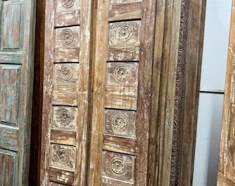 May include: A collection of weathered wooden doors. The doors are a mix of light and dark brown, with carved floral designs in rectangular panels. Some doors have a distressed, aged appearance with visible wood grain.