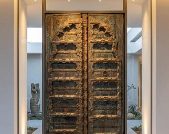 May include: A pair of tall, weathered wooden double doors featuring a dark brown finish with hints of teal patina. The doors have a rectangular panel design, arched top sections, and a central vertical beam with a small metal ring handle.