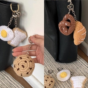 Könnte beinhalten: Gehäkelte Lebensmittel-Anhänger für eine Tasche oder einen Schlüsselanhänger. Die Anhänger umfassen ein Spiegelei und Toast, ein Brezel und Brot sowie einen Schokoladenkeks.