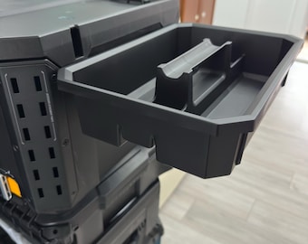 以下が含まれることがあります： 積み重ね可能なデザインの黒いモジュラー式ツール収納システム。中央にハンドルと仕切りを備えた、取り外し可能なオープンタイプのプラスチック製トレイが外側に引き出されています。本体側面には通気用のスロットが配置されています。