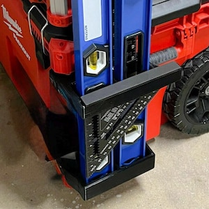Peut inclure: Un niveau et un outil de mesure d'angle bleus et noirs sont fixés à une boîte à outils roulante rouge. Le niveau a un indicateur à bulle jaune. La boîte à outils a une roue noire et le texte "Milwaukee PACKOUT".