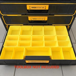 May include: A black and yellow modular storage drawer unit featuring the text TOUGHSYSTEM 2.0 on the handle. The open drawer contains multiple yellow plastic bins arranged in a grid pattern for organising small parts and hardware components.