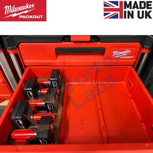 Peut inclure: Boîte à outils rouge Milwaukee Packout avec un tiroir ouvert, révélant quatre batteries rouges et noires à l'intérieur. Le tiroir est divisé en quatre sections.