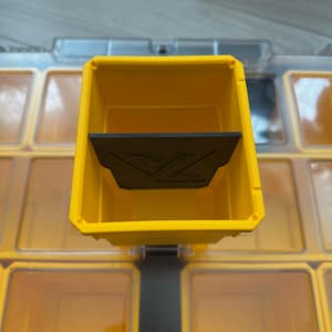 May include: A yellow plastic storage bin with a black divider and a logo. The bin is part of a larger storage system with multiple compartments. The compartments are transparent and orange.