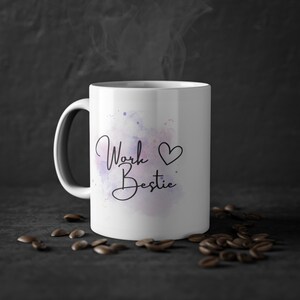 Könnte beinhalten: Weiße Keramiktasse mit einem Aquarelldesign in Lila- und Rosatönen. Die Tasse trägt den Text "Work ♥ Bestie" in schwarzer Schrift.