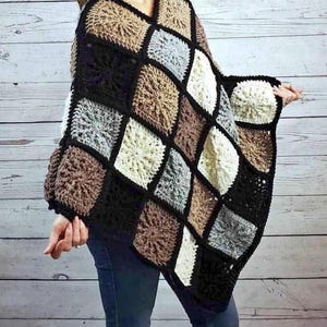 May include: A handmade crochet poncho featuring a diamond pattern in shades of black, brown, beige, and gray. The poncho has a V-neck design and is made with a textured stitch, offering a cozy and stylish look. The sleeves are also crocheted.