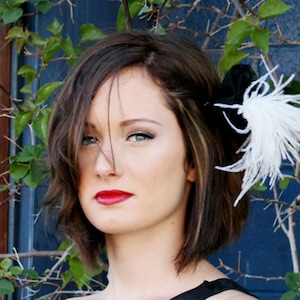 Puede incluir: Una mujer con el pelo corto y castaño lleva una pinza para el pelo de plumas blancas y negras. La pluma es blanca y la pinza es negra.