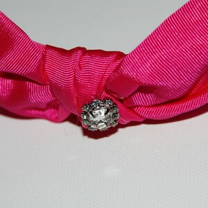 May include: A pink fabric headband with a clear rhinestone in the center.