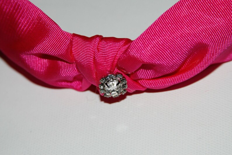 May include: A pink fabric headband with a clear rhinestone in the center.