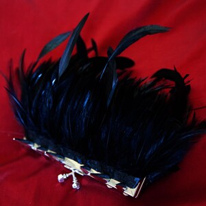 May include: A black feather clutch purse with a silver clasp. The clutch is on a red background.