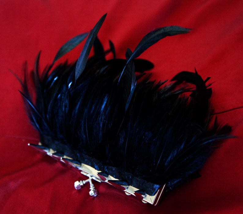 May include: A black feather clutch purse with a silver clasp. The clutch is on a red background.