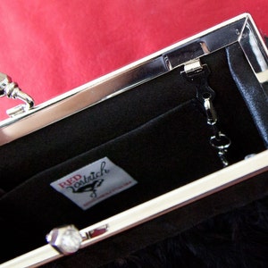 May include: A black clutch purse with a silver clasp and a silver chain. The purse has a black feather trim and a label that reads "Red Patrich".