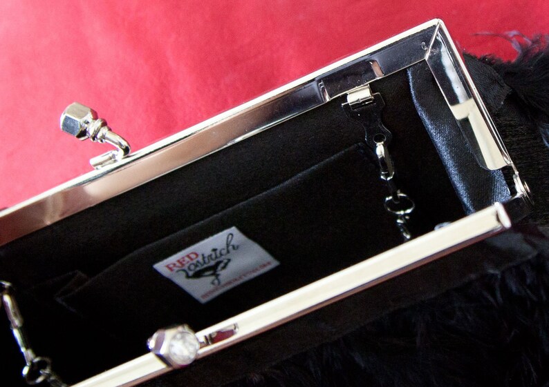 May include: A black clutch purse with a silver clasp and a silver chain. The purse has a black feather trim and a label that reads "Red Patrich".