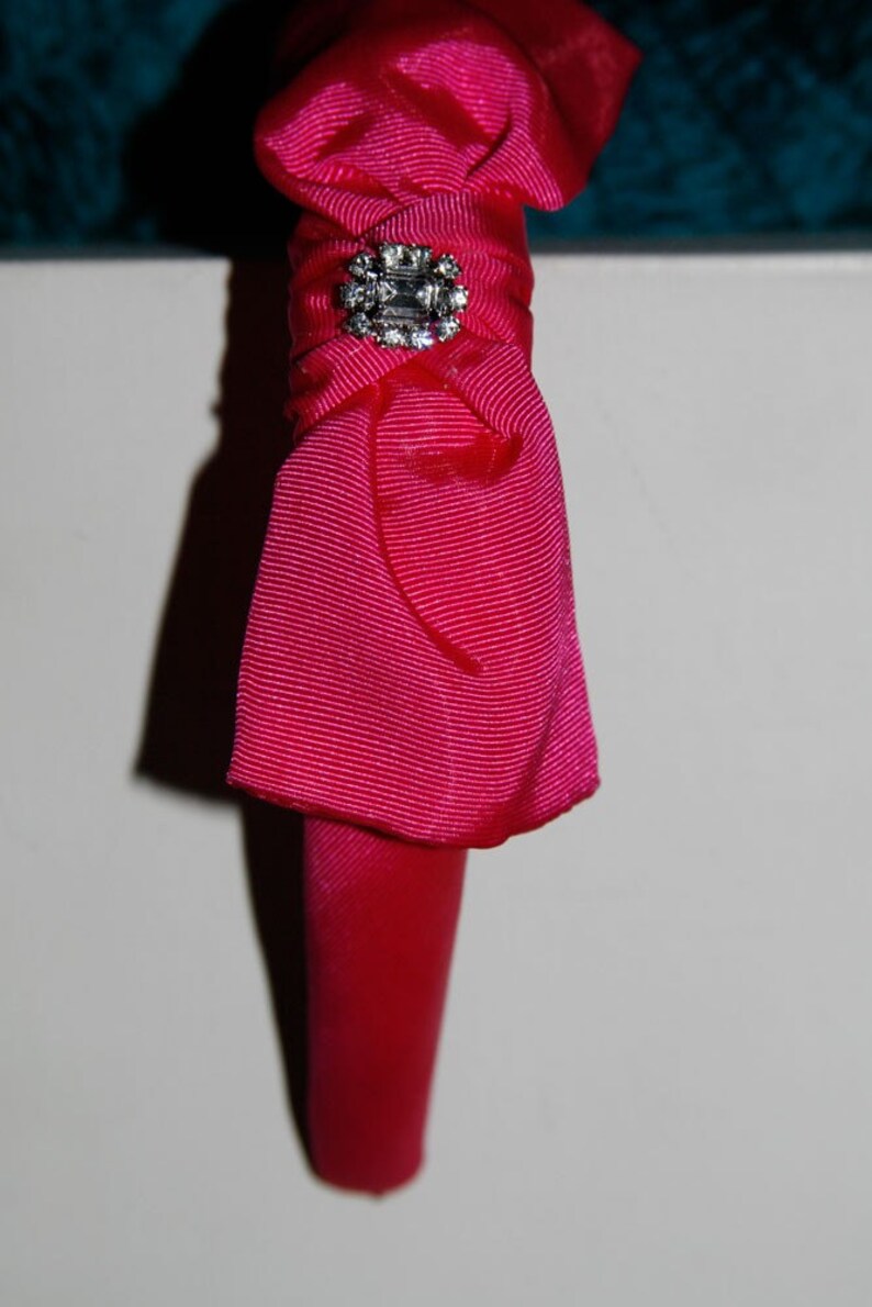 May include: A pink fabric headband with a rhinestone embellishment.