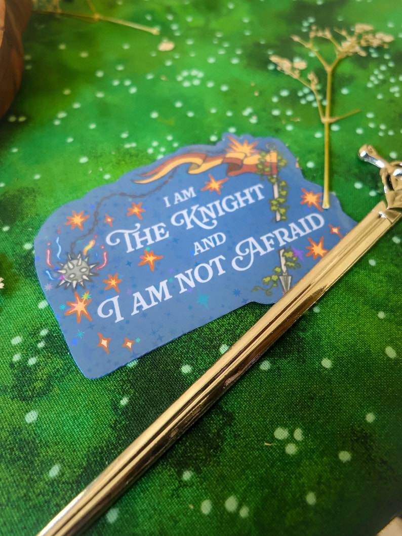 May include: A blue sticker with a glittery finish and a white border. The sticker features a knight with a sword and a banner that reads "I am the Knight and I am not afraid".