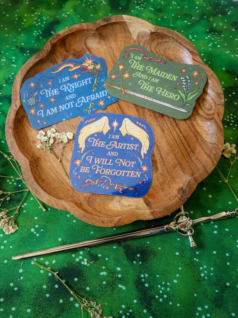 May include: Three blue, green, and purple stickers with inspirational quotes. The stickers feature a knight, a maiden, and an artist. The quotes are "I am the knight and I am not afraid", "I am the maiden and I am the hero", and "I am the artist and I will not be forgotten".