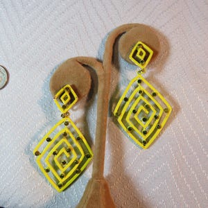 May include: A pair of yellow dangle earrings with a geometric design. The earrings are made of plastic and have a shiny finish.