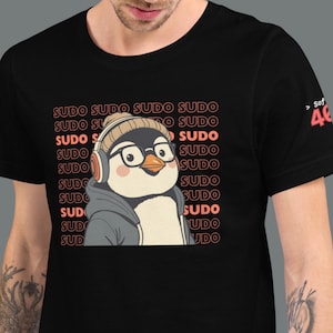 Può includere: T-shirt nera con un pinguino dei cartoni animati con cuffie e occhiali. Il pinguino è circondato dalla parola "SUDO" in un motivo ripetuto. La maglietta ha un girocollo e maniche corte.