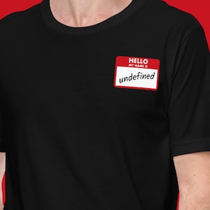 Puede incluir: Camiseta negra con una etiqueta roja y blanca que dice "HELLO MY NAME IS undefined". La etiqueta es rectangular con esquinas redondeadas. La camiseta es lisa y tiene mangas cortas.