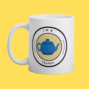 Peut inclure: Mug en céramique blanche avec une illustration de théière bleue dans un cercle. Le texte "I'M A TEAPOT" est imprimé autour de l'illustration. La tasse a une anse blanche et est posée sur un fond jaune.