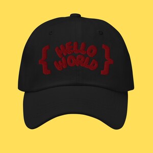May include: Black baseball cap with the embroidered text "HELLO WORLD" in red. The text is stylized with a curly font and enclosed by red brackets. The cap has a curved brim and a button on top.