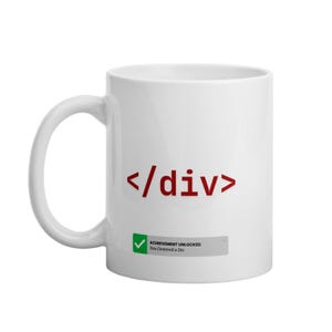 Könnte beinhalten: Weiße Keramik-Kaffeetasse mit rotem "</div>"-Design. Unter dem Text befindet sich eine kleine Grafik mit der Aufschrift "ACHIEVEMENT UNLOCKED You Centered a Div". Die Tasse hat einen gebogenen Henkel.