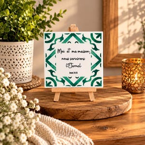 Peut inclure: Un carreau en céramique blanc de forme carrée avec une bordure décorative verte et le texte noir suivant : Moi et ma maison, nous servirons l'Éternel, Josué 24:15. Le carreau est présenté sur un petit chevalet en bois au design épuré.