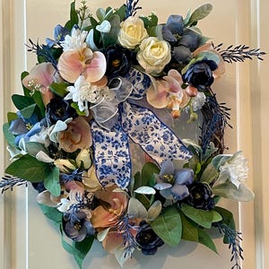 Corona romántica de verano en tonos pastel con orquídeas rosas y flores azules.