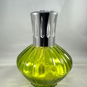 May include: A decorative glass fragrance lamp with a bright green, ribbed body and a shiny silver metal top. The lamp has a rounded, bulbous shape and a textured base. The top features vertical cutouts.