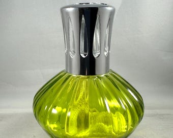Könnte beinhalten: Eine dekorative Duftlampe aus Glas mit einem hellgrünen, gerippten Körper und einem glänzenden silbernen Metallaufsatz. Die Lampe hat eine abgerundete, bauchige Form und einen strukturierten Sockel. Der Aufsatz hat vertikale Aussparungen.